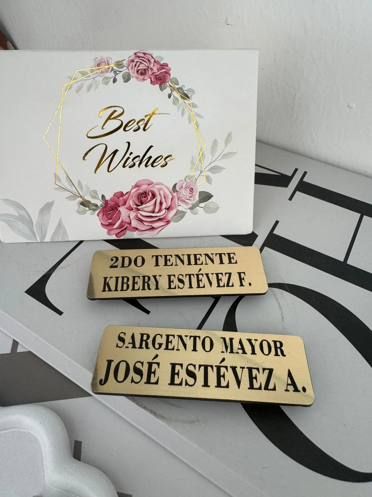 Placas metálicas doradas grabadas con rango y nombre para uniforme o credencial.